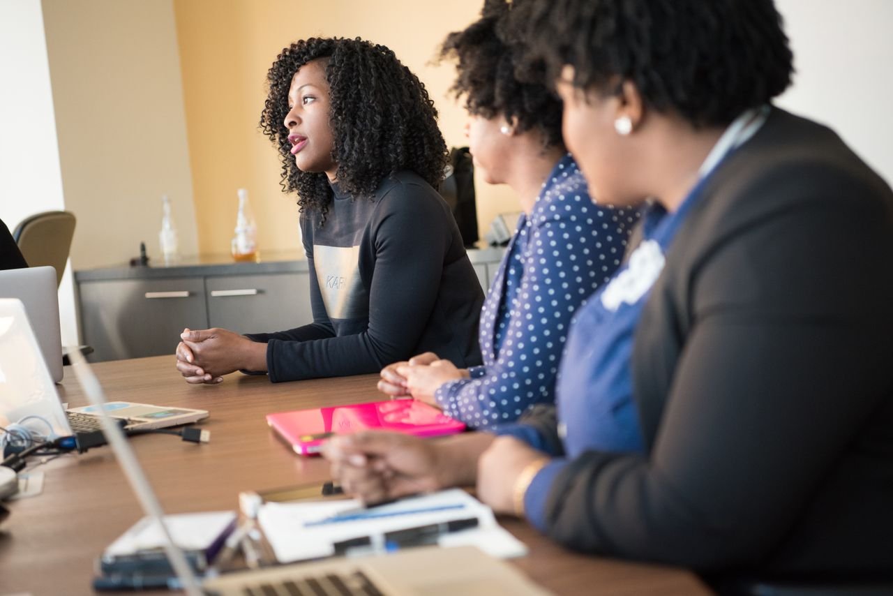 A group of women engaged in a professional meeting, collaborating in a modern office setting with laptops and documents.