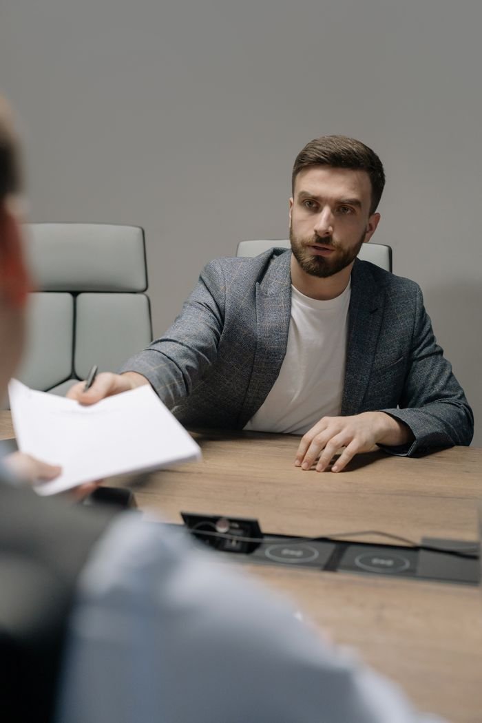 A man in a blazer negotiating across a table in a modern office setting.